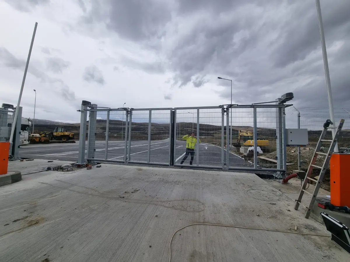 Poartă Bi-Fold V-King automatizată, zonă industrială Alba Iulia – poartă deschisă, șantier în fundal