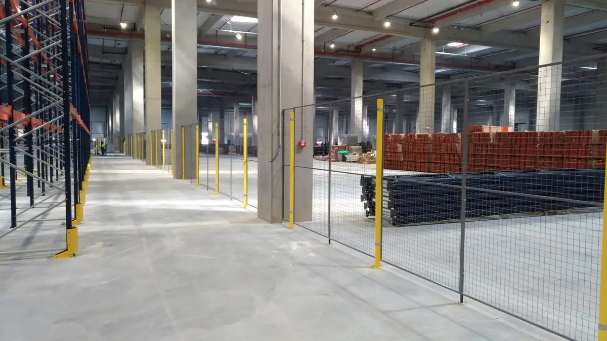 Partiționare interioară cu panouri din plasă în depozitul eMag – stâlpi galbeni, paleți cu materiale